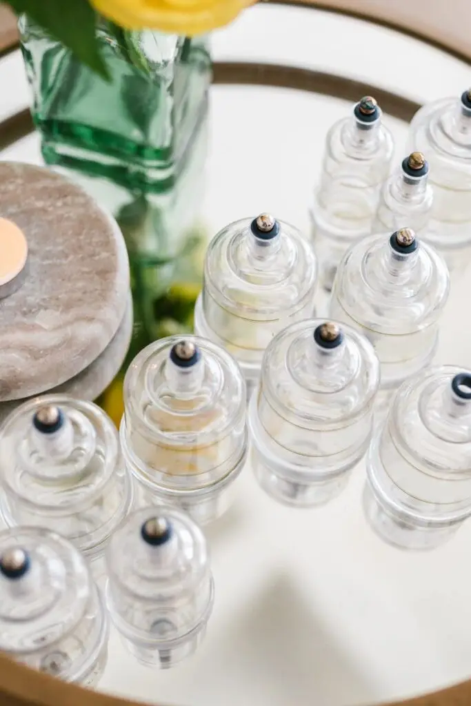 A stylish arrangement of glass cupping jars on a mirrored table with a candle and flowers, ideal for spa settings.