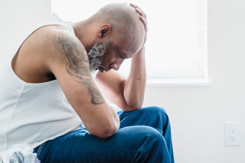 A reflective adult man with tattoos sits by a window, conveying contemplation and introspection.